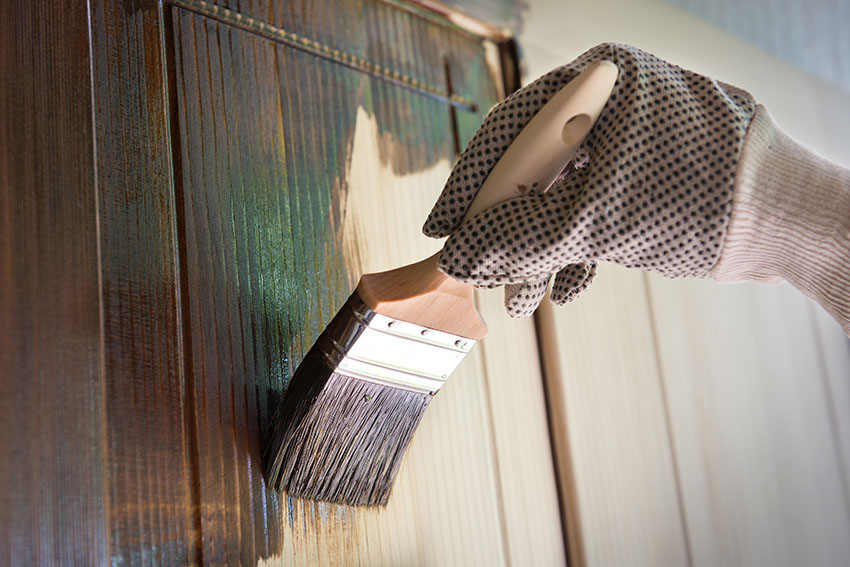 Applying wood stain on cabinet using paint brush