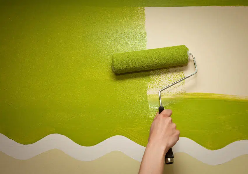 Applying green paint on a wall with paint roller