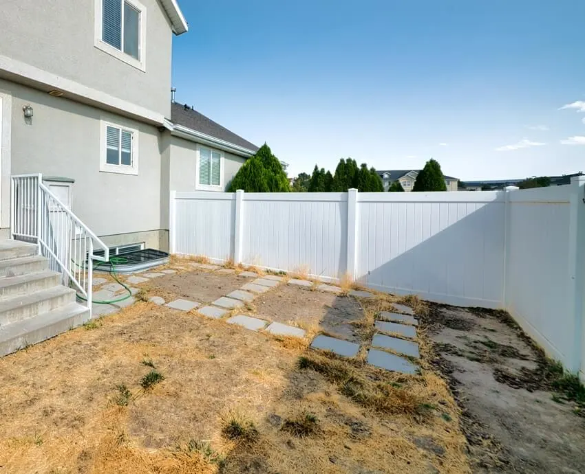 Backyard of a two storey gray house with white vinyl fence