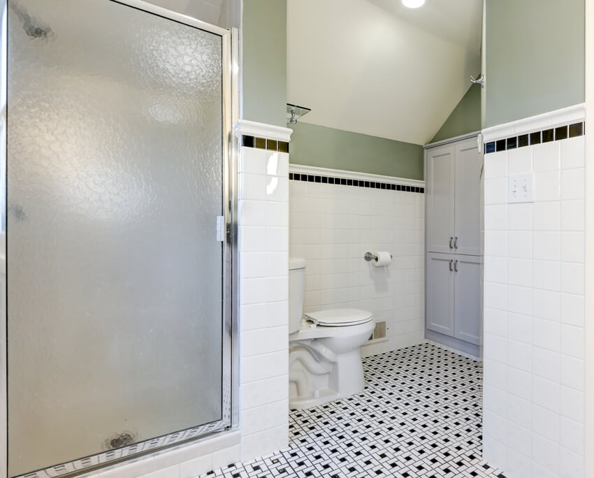 Bathroom features subway tiled half walls with black tile border over vintage black and white tile floor