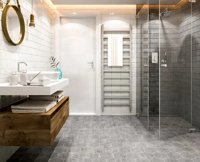 Bathroom with gray hexagonal tiles glass shower door round mirror sink wood drawer