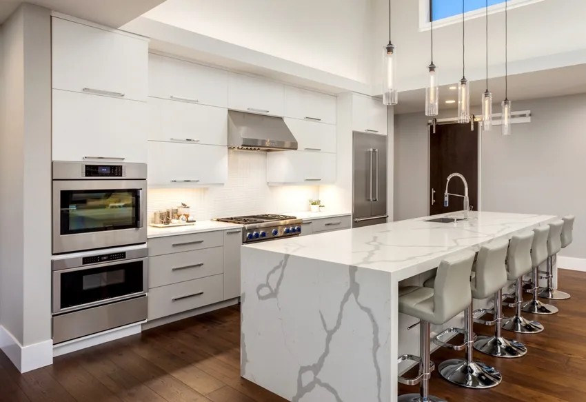 A beautiful modern kitchen with large waterfall island double ovens and hardwood floors