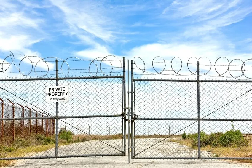 Closed gate with a chain and several padlocks and a private property sign hanging on a metal fence