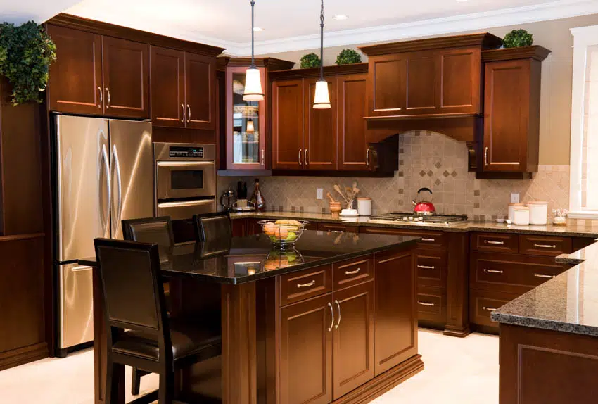 Kitchen with dark maple cabinets, tile backsplash, countertops, island, refrigerator, pendant lights, and chairs