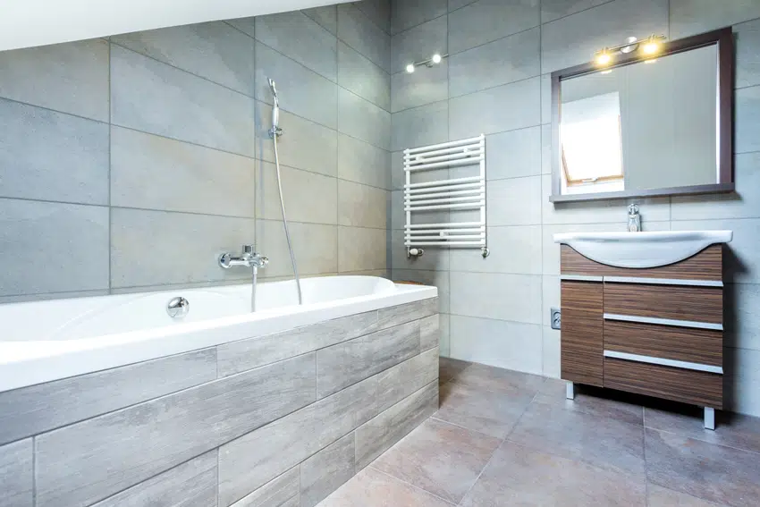 A fully tiled bathroom interior with bath and wooden shelf