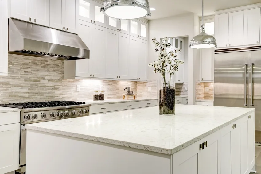 A gourmet kitchen features white shaker double stacked cabinets with marble countertops and white kitchen island