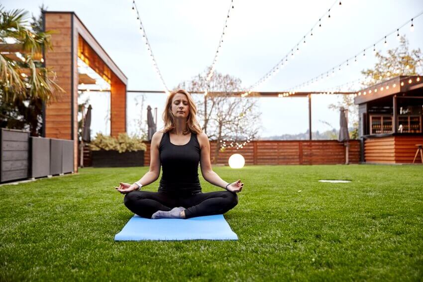 A lady meditating on yoga mat at the backyard of a fancy house