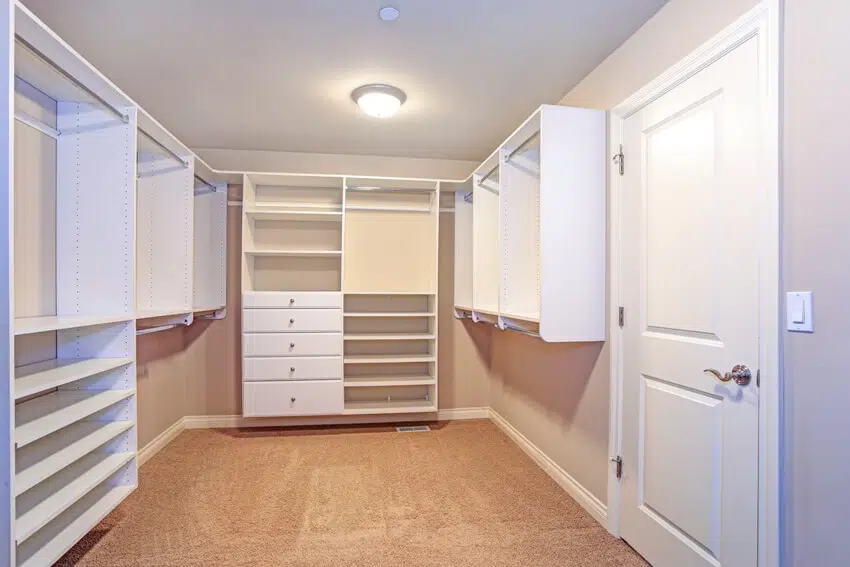 A large designed closet lined with built in drawers clothes rails and shelving over light brown carpet floor