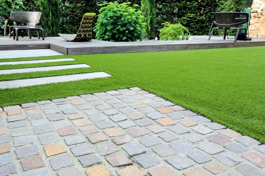 Modern garden design and terrace construction with a material mix of belgian cobble paving stones and concrete paving slab and artificial lawn and wood