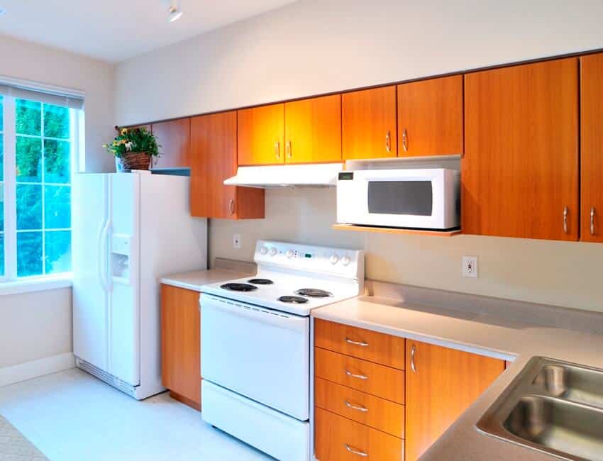 Small space kitchen with an outside view from the window wood cabinets and white appliances