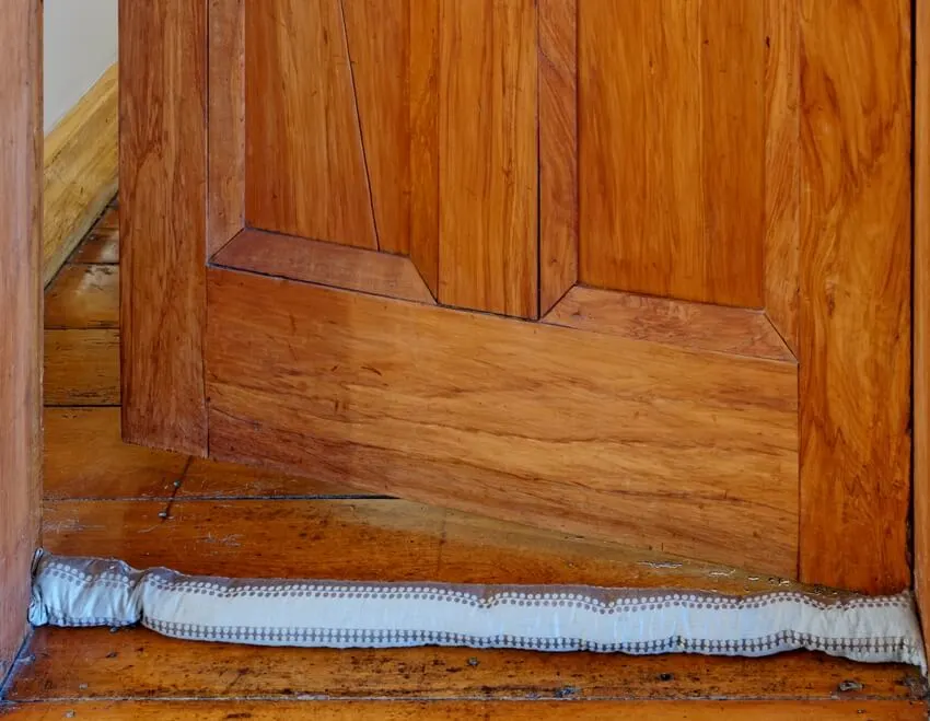 A weather-stripping draught sausage sits on the wooden floor