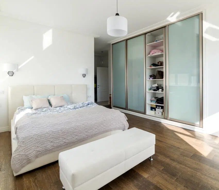 A white sunny bedroom with sliding wardrobe and wooden floors