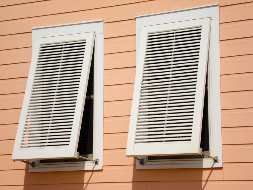 White vertical hurricane shutters on orange house siding