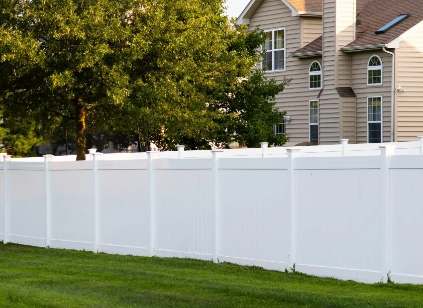 White vinyl fence outdoor backyard home with surrounding trees and green grass