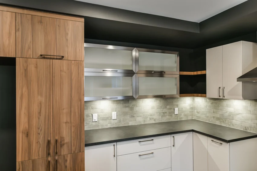 Kitchen with wood cabinets, black granite countertop, under-cabinet lighting, and subway backsplash