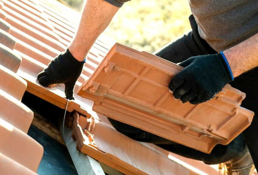 Worker hands installing yellow ceramic roofing tiles mounted on wooden boards covering residential building roof