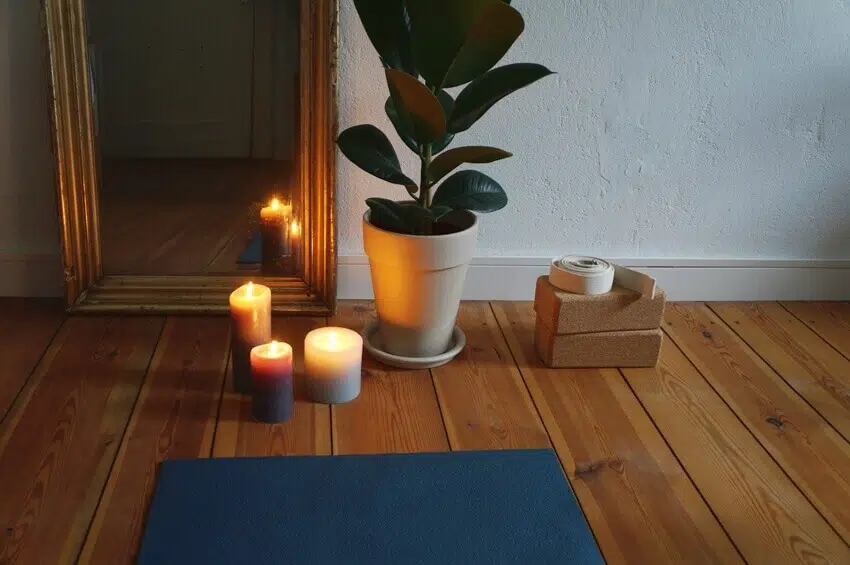 Yoga mat on wooden floor with candles mirror yoga blocks plant in the background