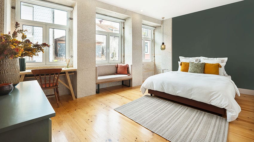 Bedroom with wooden flooring green accent wall paint rug casement windows pendant light