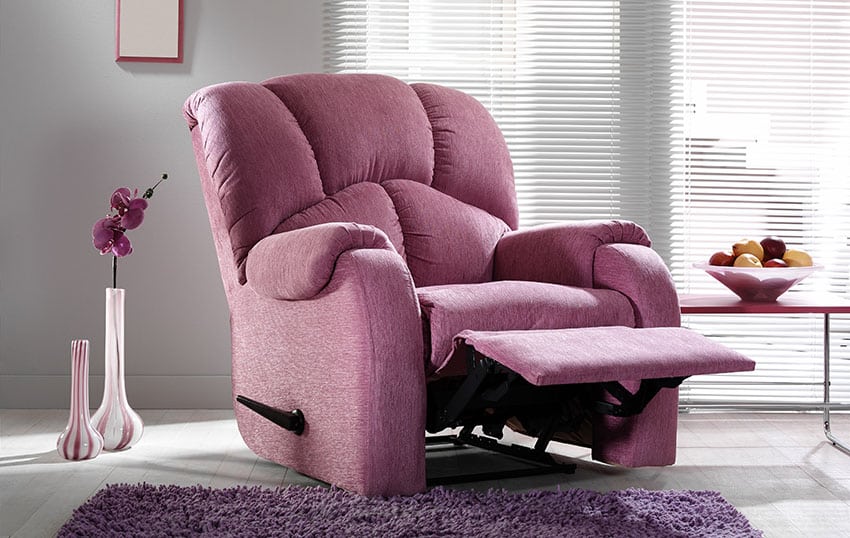 Living room with large pink recliner chair, rug, window blinds, and side table