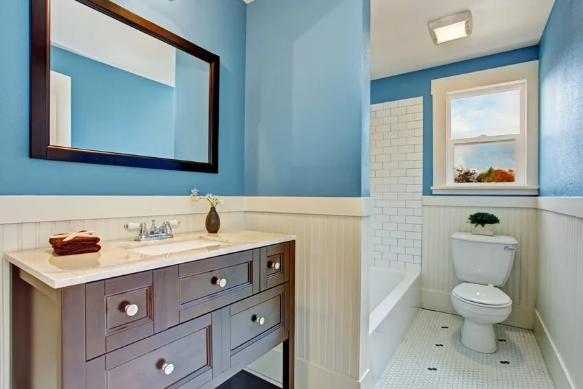 Bathroom interior with blue wall and white plank panel trim bath tub with tile wall trim and brown vanity cabinet with mirror