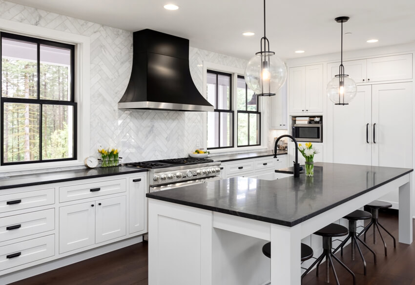 Beautiful kitchen in new luxury home with white cabinets and black accents including black island countertop and backsplash