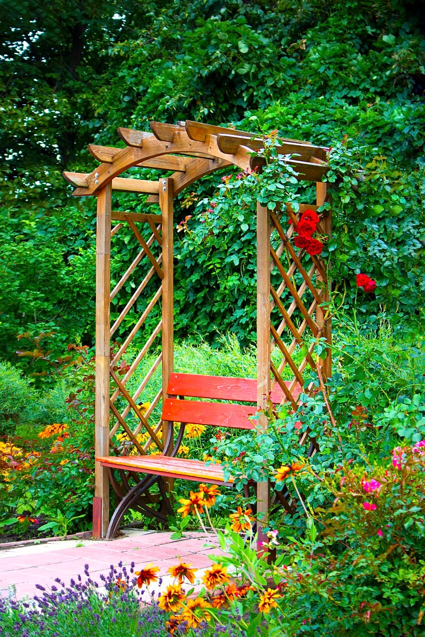 Beautiful wooden alkove in green summer garden with bright flowers
