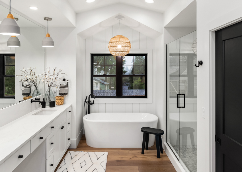 Black and white bathroom bathtub wood flooring black windows mirror sink drawers door