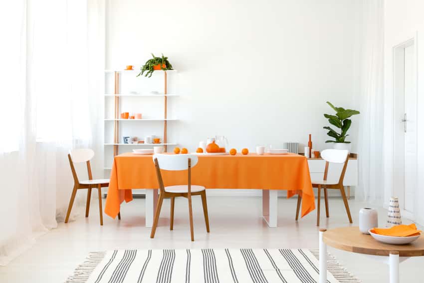 Bright and spacious dining room rectangular table orange tablecloth chairs rug indoor plant