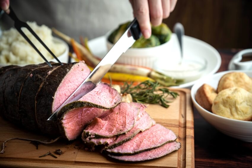 Carving roast beef on a cutting board with knife and fork