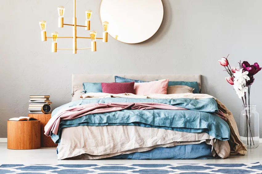 Circular mirror hanging above large bed with teal and pastel pink sheets and pillows