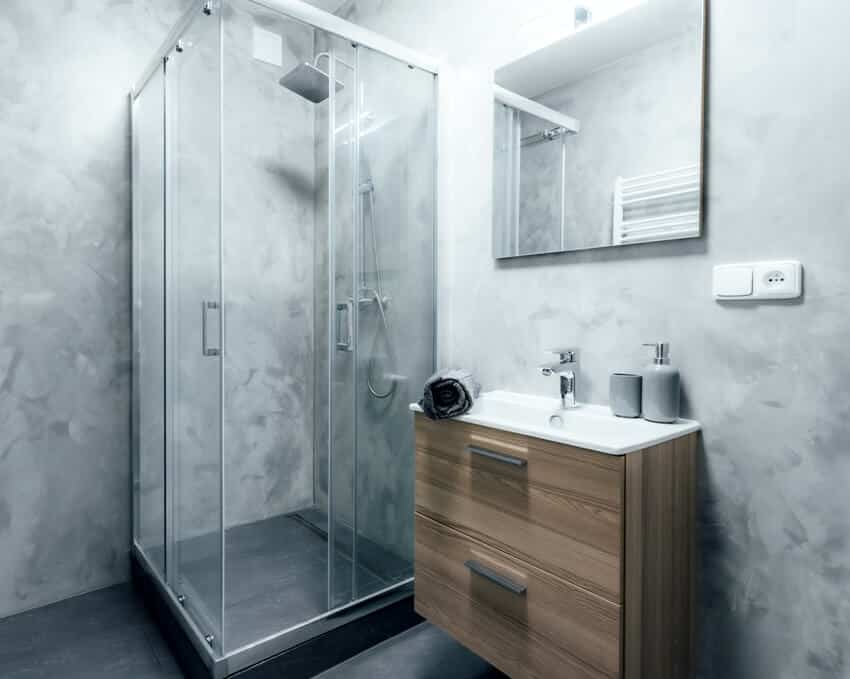 Contemporary bathroom with smooth stucco wall finish shower and sink with wooden cabinet under it and mirror with integrated light