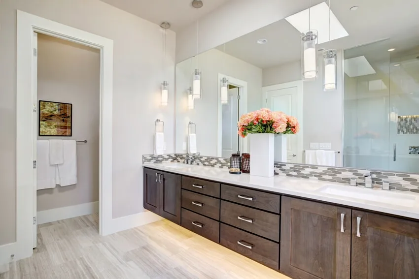 Contemporary master bathroom features a dark dual vanity cabinet and white countertop with mosaic backsplash under a large full mirror