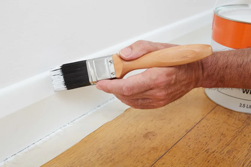 Contractor painting baseboard same color as wall wood flooring