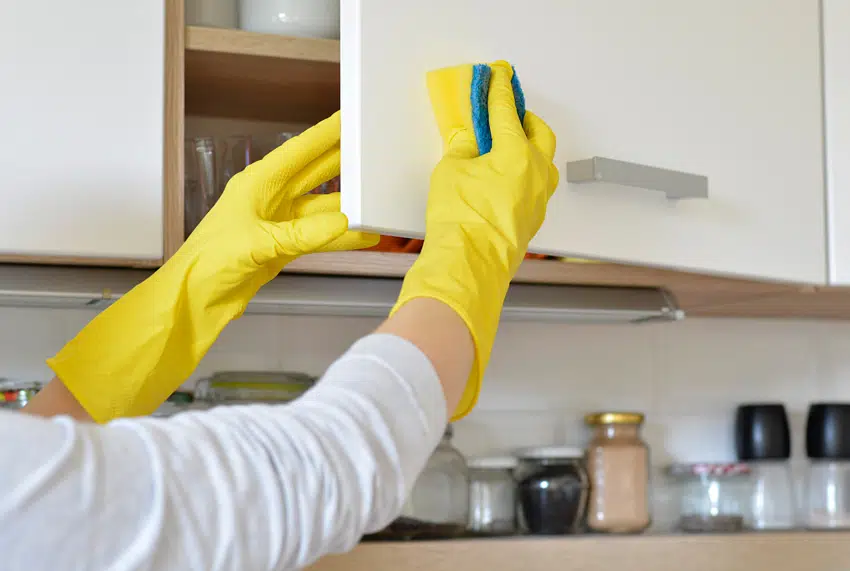 Individual with a yellow glove cleaning a cabinet