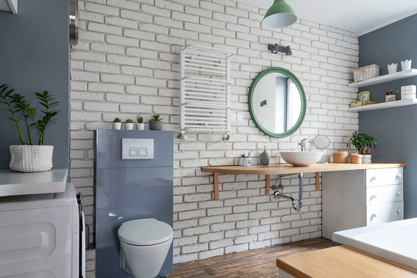 Interior of industrial bathroom in loft apartment with brick wall, grey decor, round mirror and wooden furniture 