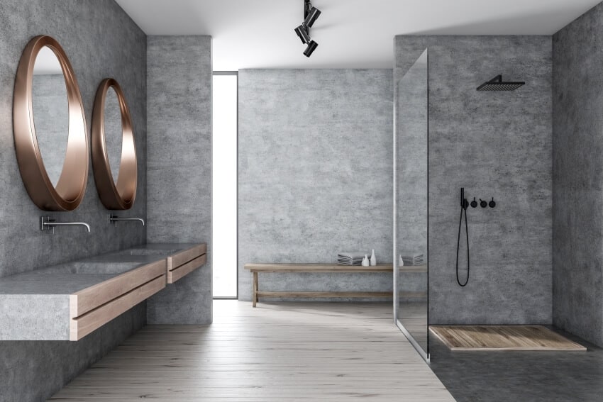 Interior of modern bathroom with shower stall with glass wall concrete walls wooden floor double sink with two round mirrors and bench with towels