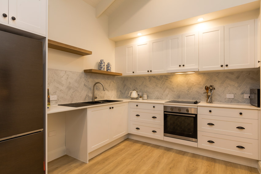 Kitchen with backsplash tile herringbone, white cabinets, floating shelves, and wood flooring