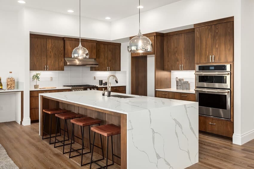 Kitchen in new luxury home with island pendant lights, quartz waterfall island with dark cabinets and stainless steel appliances