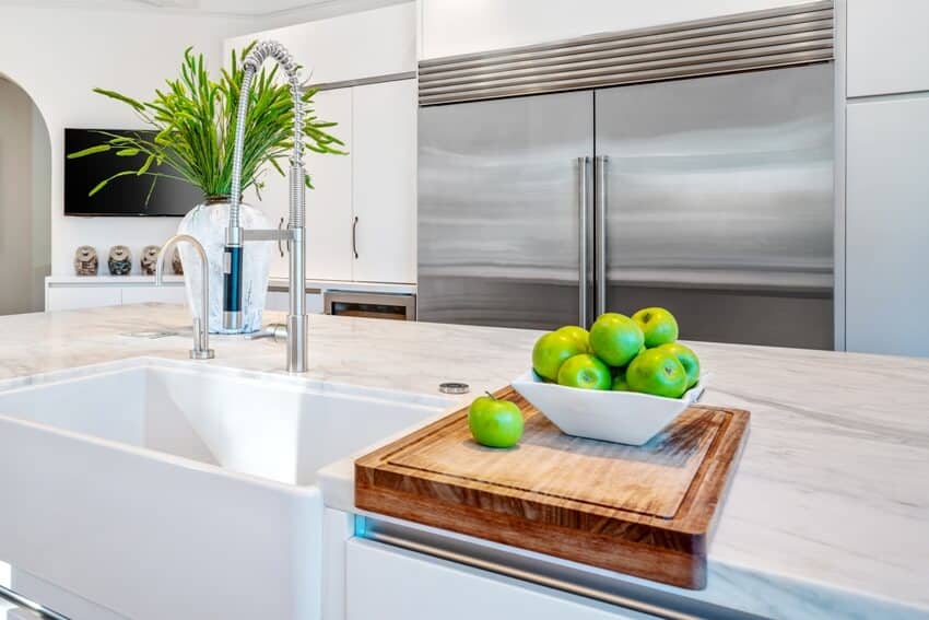 Kitchen with white cabinets and center island with wood cutting board and a bowl of green apples