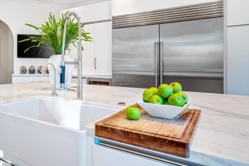 Kitchen with white cabinets and center island with wood cutting board and a bowl of green apples 