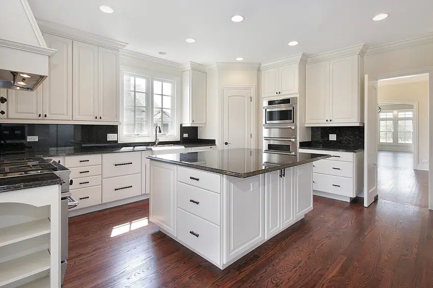 Kitchen with white cabinets, wood flooring, black countertop, center island glass windows