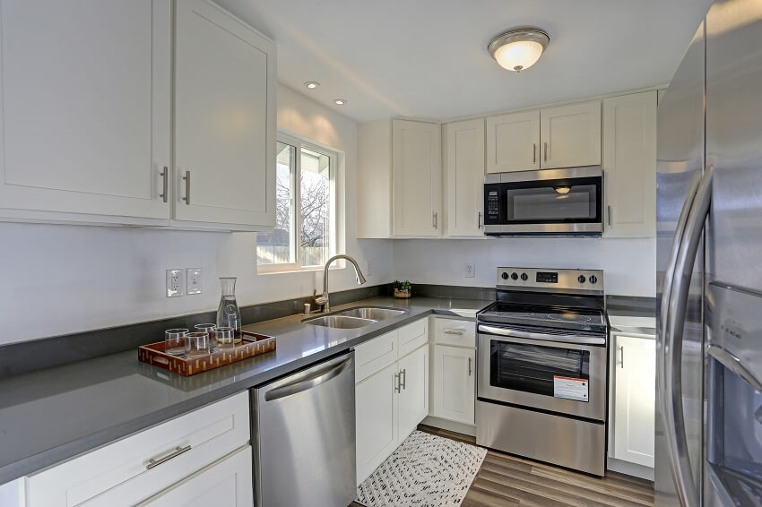 Light filled home interior features small compact kitchen with white cabinets and modern stainless steel appliances