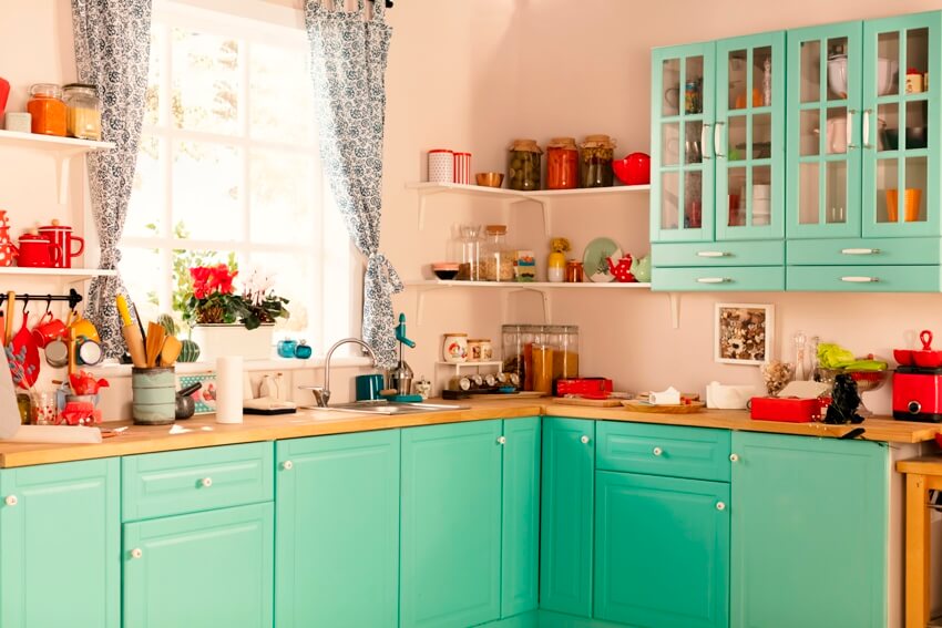 Light sage green wooden kitchen with window and colorful decors and accents 