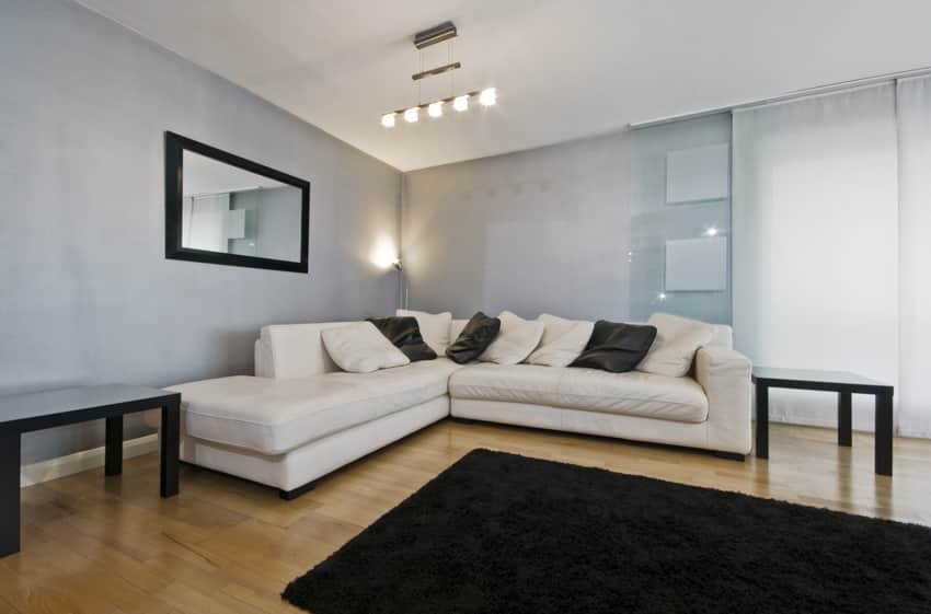Living room with white leather couch, wood floor, side tables, track lighting, rug, pillows, and mirror
