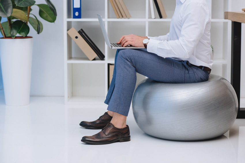 Man sitting on exercise ball while working shelf white floor