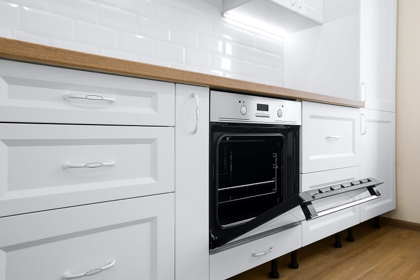Modern cooking stove in white kitchen interior with tiled wall and wooden countertop