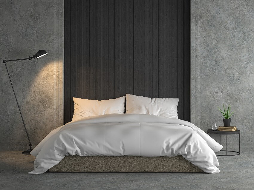 Modern loft bedroom with black wood plank polished concrete wall and floor furnished with brown fabric bed and white blanket and industrial style lamp