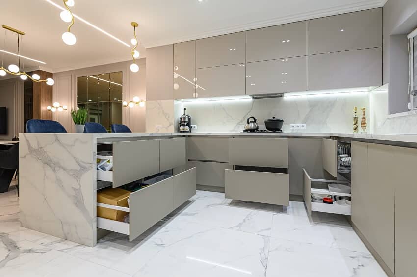 Open drawers at well designed large modern white wood and marble kitchen united with living room