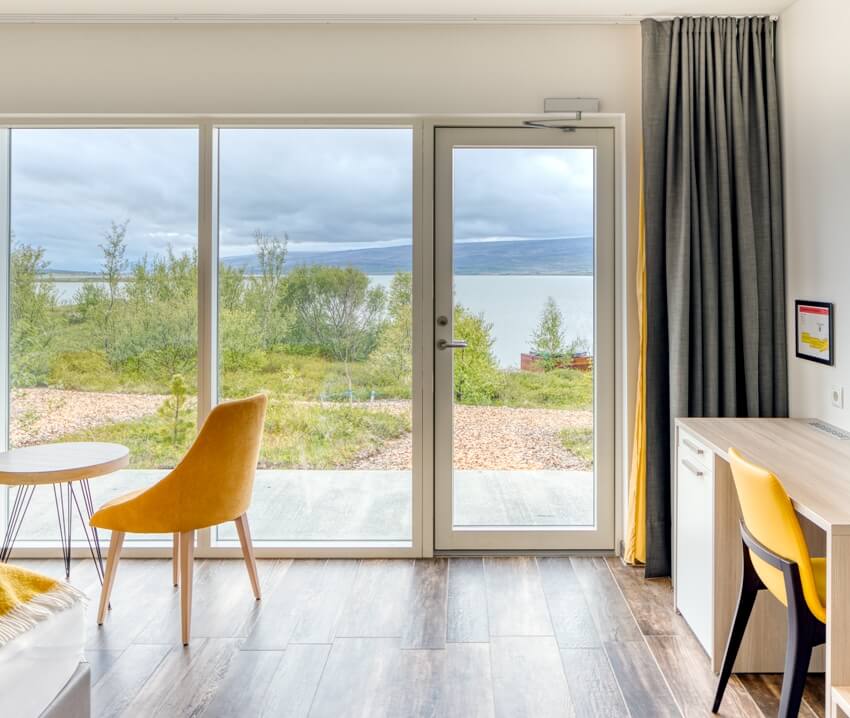 Outside views from inside a modern minimalist room with chairs wooden tile floor and closed glass hinge door