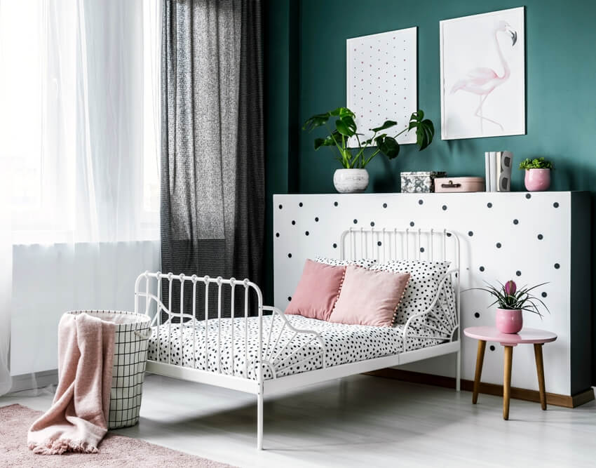 Pink flower on table next to white bed with foot railings 